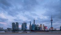 the skyline is lit up at dusk near the water and buildings with a long line of people waiting