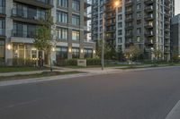 an empty street lined with tall buildings at dusk over a green field with some grass