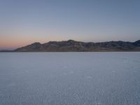 snow is in the middle of a barren plain, at dusk, near mountains and water