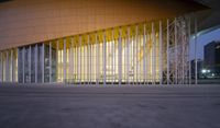 a building with glass and metal columns at dusk with light from outside the building in front