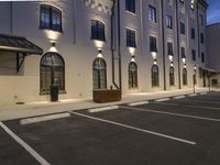 the car park of an outdoor business center at dusk in a large building lit by street lamps