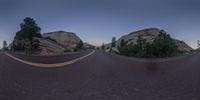 a fish eye lens shot showing the road passing in front of two large rocks at dusk