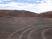 a dirt field with tires going through it, and hills in the distance in the background