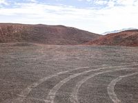 a dirt field with tires going through it, and hills in the distance in the background