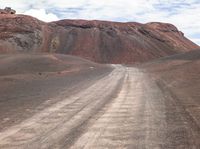 a lone truck driving down a dusty road in the mountainside to a hill covered by red dirt