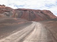 a lone truck driving down a dusty road in the mountainside to a hill covered by red dirt