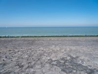 a blue kite is flying in the air near the ocean and water to shore, as people are relaxing on an empty beach