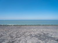 a blue kite is flying in the air near the ocean and water to shore, as people are relaxing on an empty beach