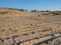 sand and grass on a beach with fence in the background near to it and small rock formations and sand mounds