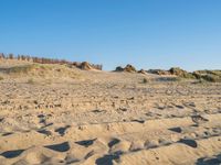 sand and grass on a beach with fence in the background near to it and small rock formations and sand mounds