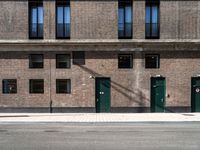 three doors sit outside of a brick building on the corner of a street and sidewalk