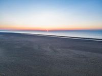 the sunset is setting over the water in this photograph on a beach area with a bench in front