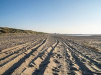 a sandy beach with a path and truck tracks in the sand, with many small vehicles on the side of it