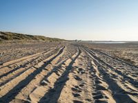 a sandy beach with a path and truck tracks in the sand, with many small vehicles on the side of it