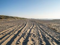 a sandy beach with a path and truck tracks in the sand, with many small vehicles on the side of it