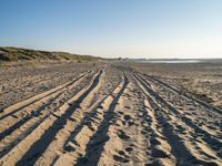 a sandy beach with a path and truck tracks in the sand, with many small vehicles on the side of it