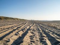 a sandy beach with a path and truck tracks in the sand, with many small vehicles on the side of it