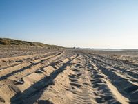 a sandy beach with a path and truck tracks in the sand, with many small vehicles on the side of it