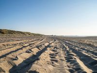 a sandy beach with a path and truck tracks in the sand, with many small vehicles on the side of it