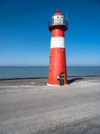 the red and white lighthouse is by the water's edge with the road beside it