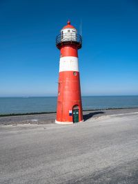 the red and white lighthouse is by the water's edge with the road beside it