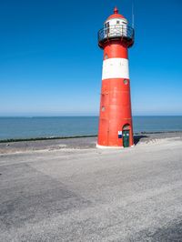 the red and white lighthouse is by the water's edge with the road beside it