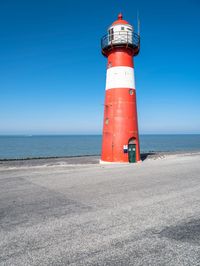 the red and white lighthouse is by the water's edge with the road beside it