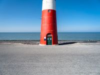 the lighthouse is sitting near the shore of the beach that stretches into the blue sea