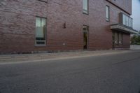 a skateboard on the street next to a brick building with windows and a yellow fire hydrant in front of it
