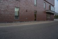 a skateboard on the street next to a brick building with windows and a yellow fire hydrant in front of it