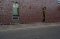 a skateboard on the street next to a brick building with windows and a yellow fire hydrant in front of it