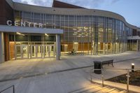 the glass entrance to martin center is illuminated by the evening sun, with some benches outside