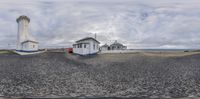 this is a photo of a lighthouse with clouds in the background and a house on the left and a small white building with a red door