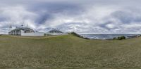 two white buildings standing on a green hillside near the ocean with clouds overhead and blue sky