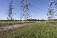 three electric towers in grassy area next to a dirt road and woodside road, with two people standing on one