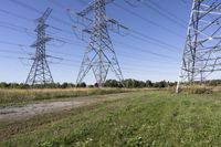 three electric towers in grassy area next to a dirt road and woodside road, with two people standing on one