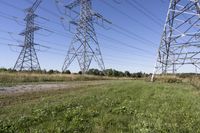 three electric towers in grassy area next to a dirt road and woodside road, with two people standing on one