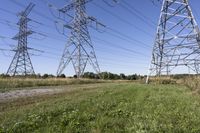 three electric towers in grassy area next to a dirt road and woodside road, with two people standing on one