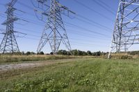 three electric towers in grassy area next to a dirt road and woodside road, with two people standing on one