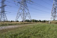 three electric towers in grassy area next to a dirt road and woodside road, with two people standing on one