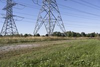 three electric towers in grassy area next to a dirt road and woodside road, with two people standing on one