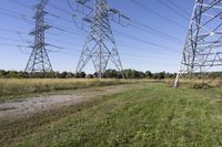 three electric towers in grassy area next to a dirt road and woodside road, with two people standing on one