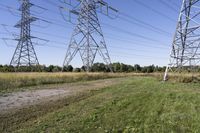 three electric towers in grassy area next to a dirt road and woodside road, with two people standing on one