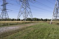 three electric towers in grassy area next to a dirt road and woodside road, with two people standing on one