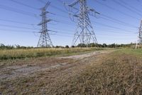 three electric towers in grassy area next to a dirt road and woodside road, with two people standing on one