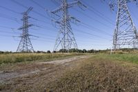 three electric towers in grassy area next to a dirt road and woodside road, with two people standing on one