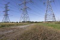 three electric towers in grassy area next to a dirt road and woodside road, with two people standing on one