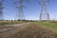 three electric towers in grassy area next to a dirt road and woodside road, with two people standing on one