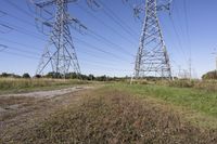 three electric towers in grassy area next to a dirt road and woodside road, with two people standing on one