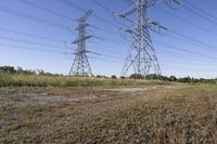 three electric towers in grassy area next to a dirt road and woodside road, with two people standing on one